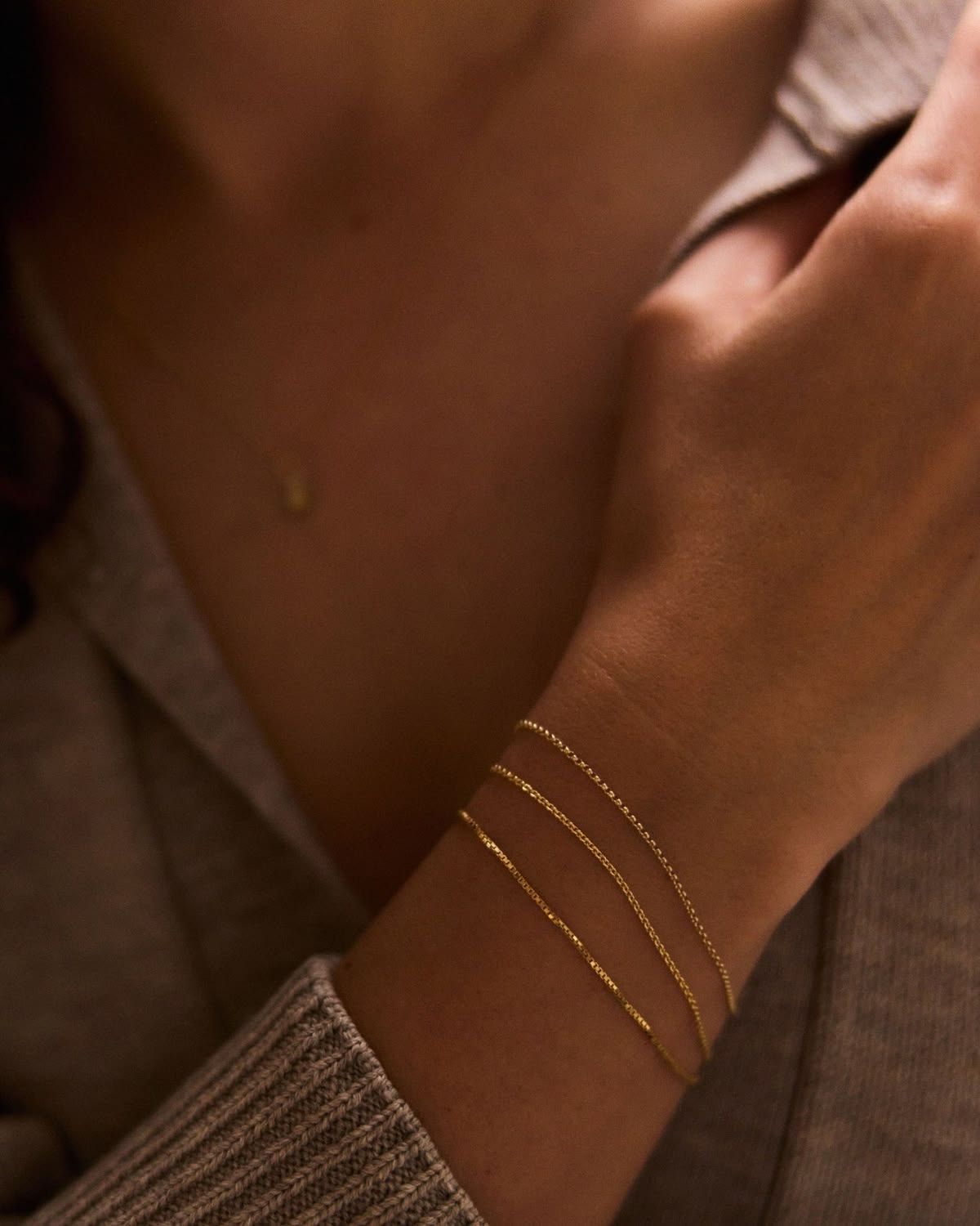 A wrist stacked with three welded gold chain bracelets